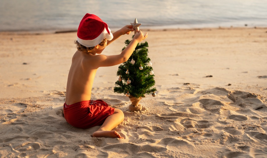 Child decorating a Christmas tree on the beach